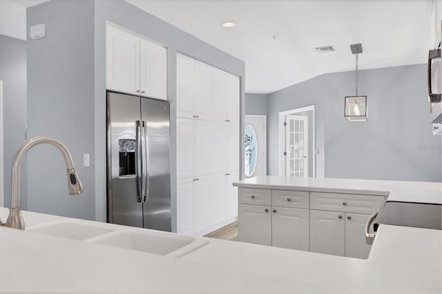 kitchen with stainless steel fridge, sink, white cabinets, and hanging light fixtures