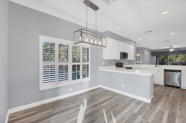 kitchen featuring white cabinetry, kitchen peninsula, decorative light fixtures, appliances with stainless steel finishes, and light wood-type flooring