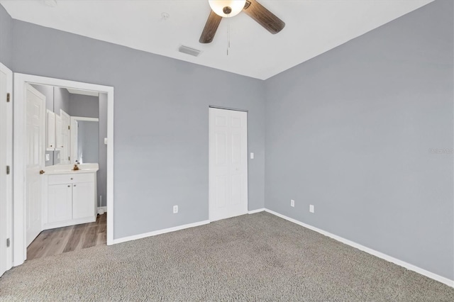 unfurnished bedroom featuring ceiling fan, light colored carpet, ensuite bath, and a closet