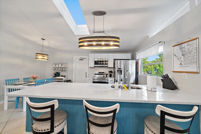 kitchen featuring light tile patterned flooring, sink, appliances with stainless steel finishes, decorative light fixtures, and white cabinets