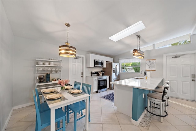 kitchen with appliances with stainless steel finishes, pendant lighting, sink, white cabinets, and lofted ceiling with skylight