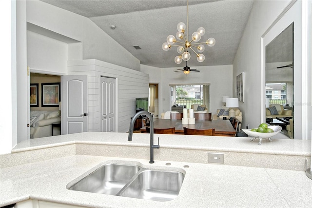 kitchen with a textured ceiling, sink, vaulted ceiling, and ceiling fan with notable chandelier