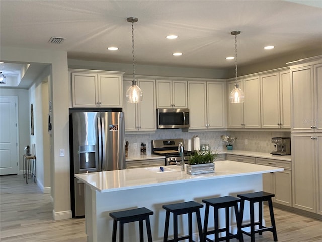 kitchen featuring appliances with stainless steel finishes, a center island with sink, and decorative light fixtures