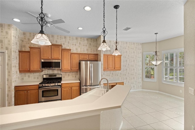 kitchen with sink, appliances with stainless steel finishes, ceiling fan, hanging light fixtures, and a kitchen island with sink