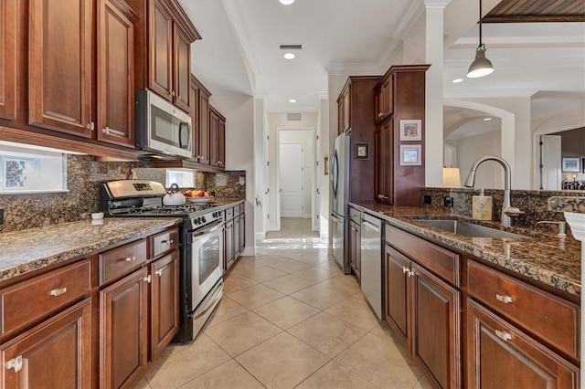 kitchen featuring sink, ornamental molding, pendant lighting, appliances with stainless steel finishes, and dark stone countertops