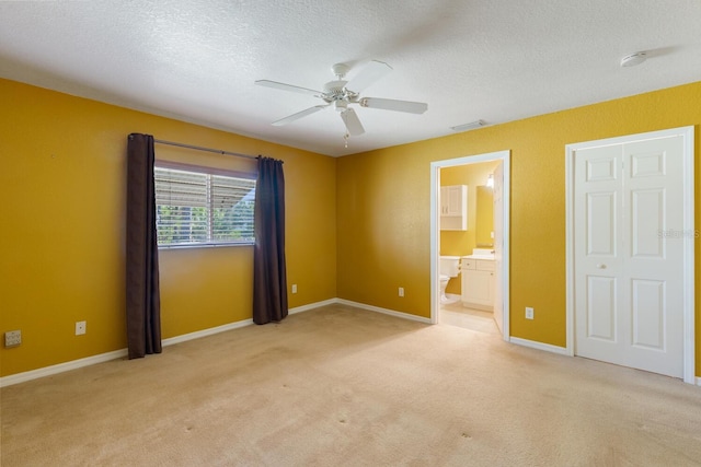 unfurnished bedroom with ensuite bathroom, a textured ceiling, light carpet, and ceiling fan