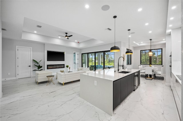 kitchen with sink, a large island, ceiling fan, a raised ceiling, and decorative light fixtures