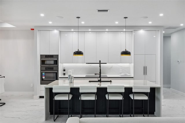 kitchen with white cabinets, an island with sink, pendant lighting, and double oven