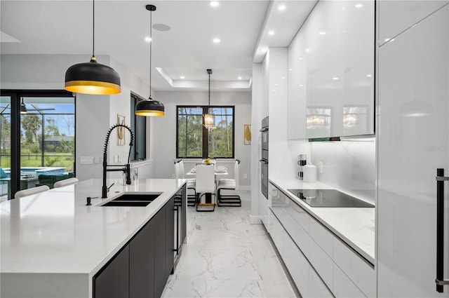 kitchen with white cabinets, black appliances, sink, a large island, and decorative light fixtures