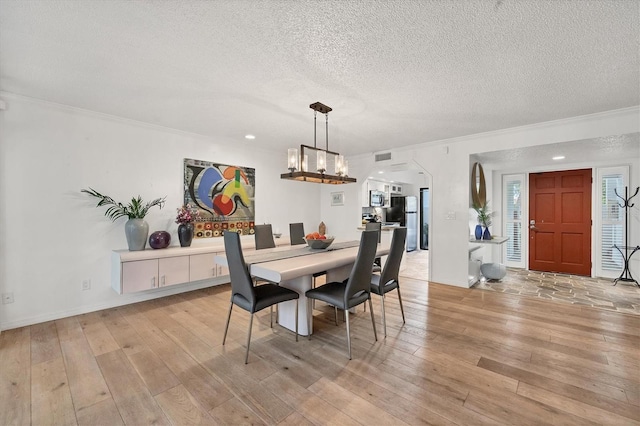 dining area with ornamental molding, light hardwood / wood-style floors, a notable chandelier, and a textured ceiling