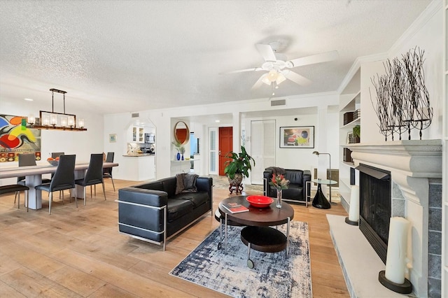 living room featuring ceiling fan with notable chandelier, a textured ceiling, ornamental molding, light wood-type flooring, and built in features