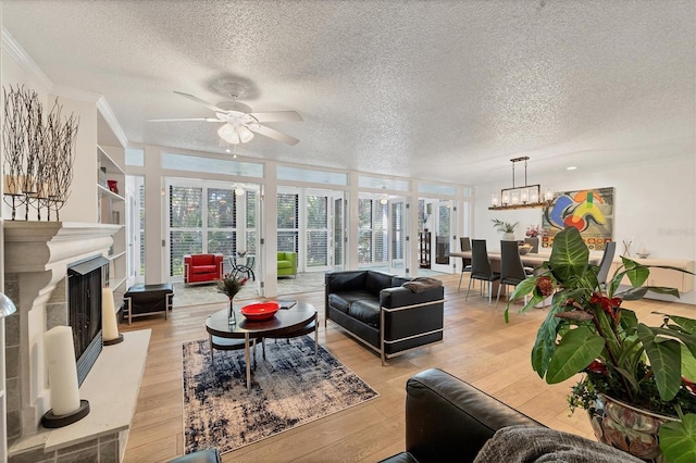 living room with ceiling fan with notable chandelier, light hardwood / wood-style floors, a textured ceiling, ornamental molding, and a wall of windows