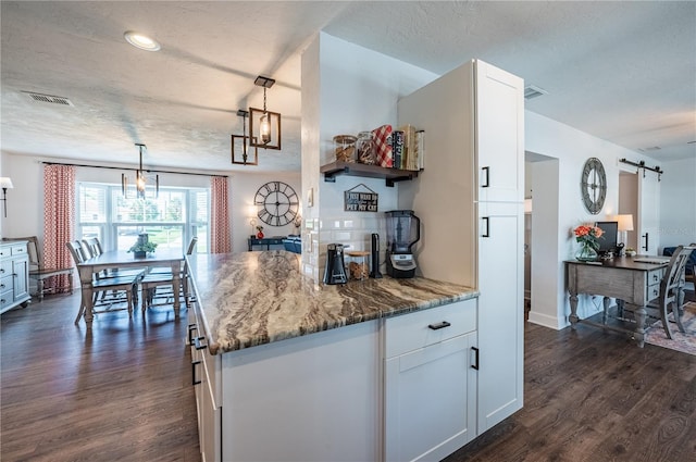 kitchen with dark wood-type flooring, white cabinetry, hanging light fixtures, and a barn door