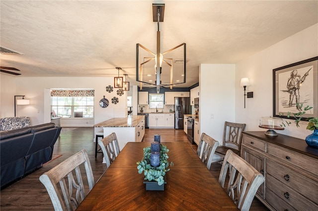 dining space with a textured ceiling, sink, an inviting chandelier, and dark hardwood / wood-style flooring