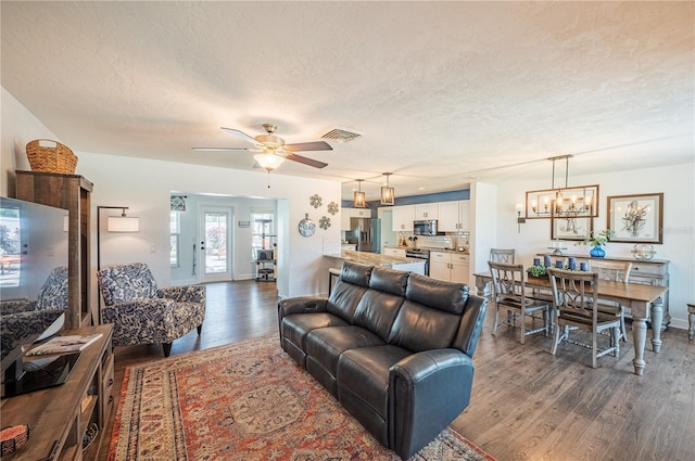 living room featuring ceiling fan with notable chandelier, a textured ceiling, and dark hardwood / wood-style flooring