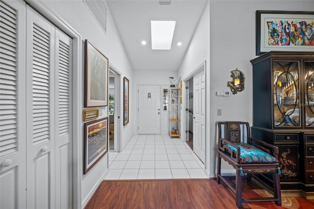 hall featuring vaulted ceiling with skylight and light wood-type flooring