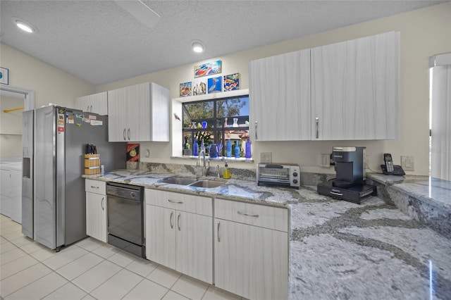 kitchen with black dishwasher, a textured ceiling, sink, light stone countertops, and stainless steel fridge