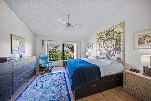 bedroom with ceiling fan, a textured ceiling, light hardwood / wood-style flooring, and lofted ceiling