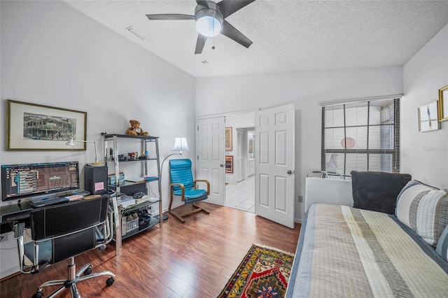 bedroom featuring ceiling fan, a textured ceiling, light wood-type flooring, and vaulted ceiling