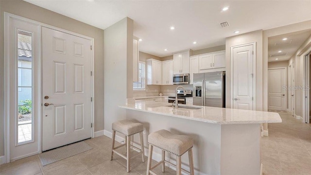 kitchen featuring stainless steel appliances, white cabinetry, sink, light stone counters, and a kitchen breakfast bar