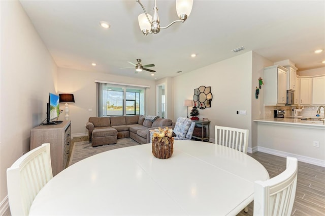 dining area featuring ceiling fan with notable chandelier, sink, and light hardwood / wood-style flooring