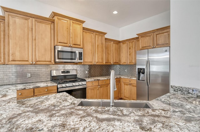 kitchen featuring tasteful backsplash, light stone counters, sink, and stainless steel appliances