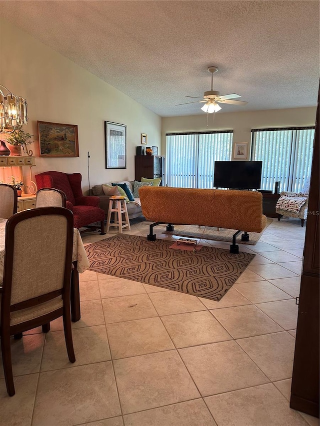 living room featuring vaulted ceiling, ceiling fan with notable chandelier, light tile patterned floors, and a textured ceiling