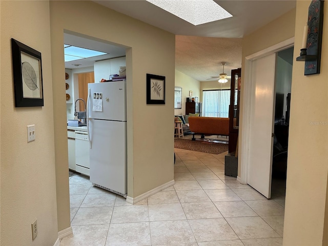 hallway with a skylight, sink, light tile patterned floors, and a textured ceiling