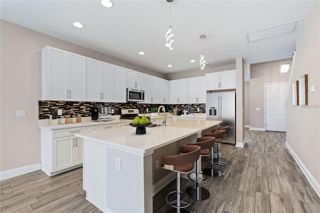 kitchen featuring white cabinetry, appliances with stainless steel finishes, decorative light fixtures, and a center island with sink