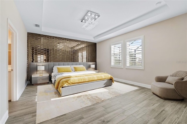 bedroom with light hardwood / wood-style flooring and a tray ceiling