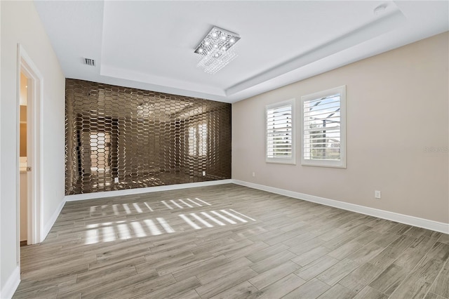 empty room featuring light hardwood / wood-style flooring, a chandelier, and a tray ceiling