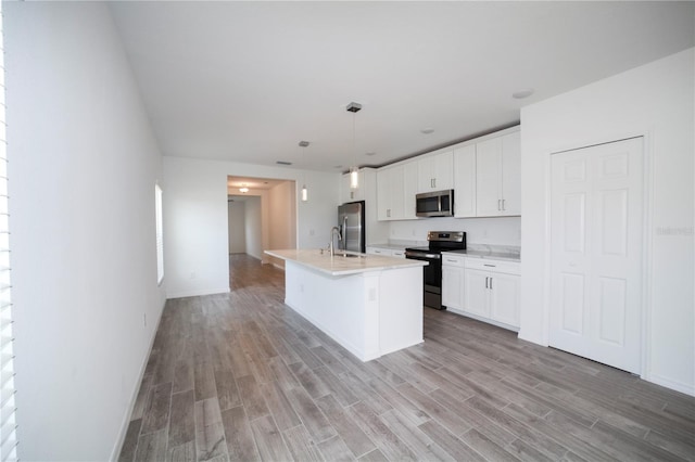 kitchen with stainless steel appliances, light hardwood / wood-style floors, white cabinetry, a center island with sink, and hanging light fixtures