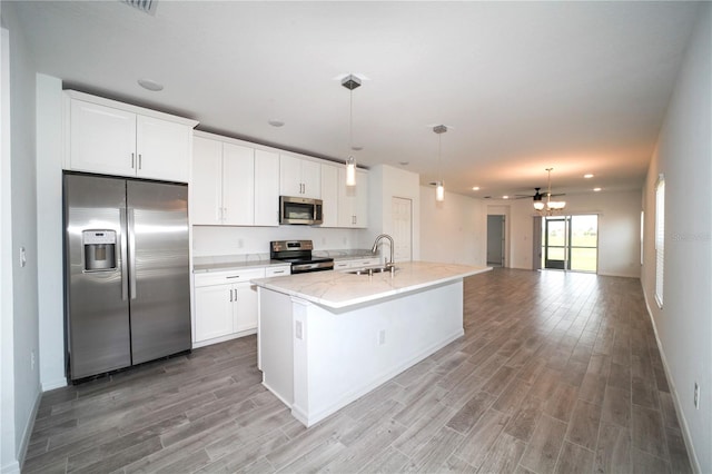 kitchen featuring stainless steel appliances, hanging light fixtures, light hardwood / wood-style floors, white cabinets, and a kitchen island with sink