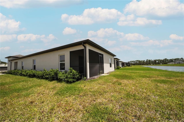 view of home's exterior with a sunroom, a water view, and a yard