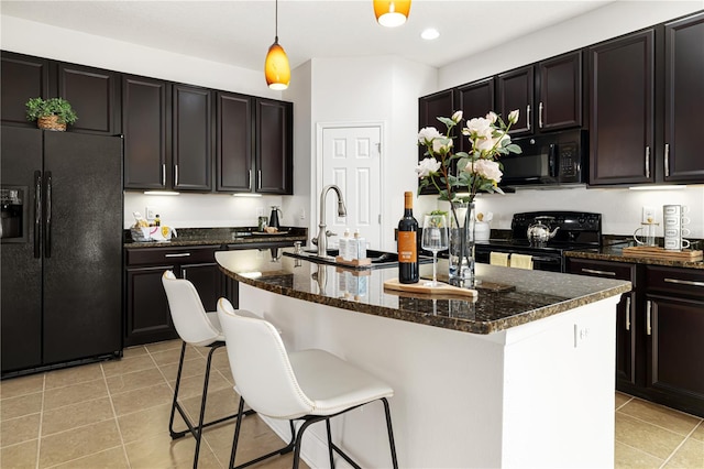 kitchen with a kitchen island with sink, black appliances, light tile patterned floors, and decorative light fixtures