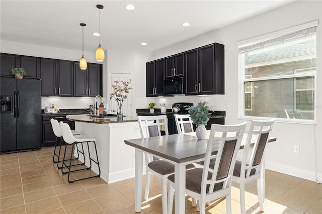 kitchen with a kitchen bar, black appliances, light tile patterned floors, a kitchen island with sink, and pendant lighting