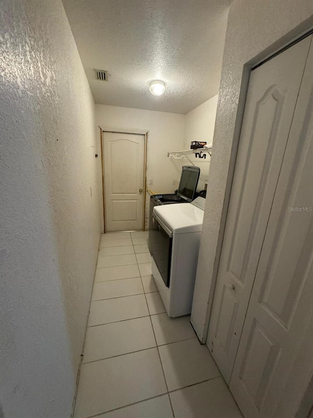 washroom with washing machine and clothes dryer, a textured ceiling, and light tile patterned floors