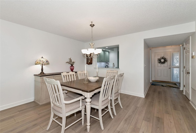 dining area with a textured ceiling, light hardwood / wood-style flooring, and a chandelier