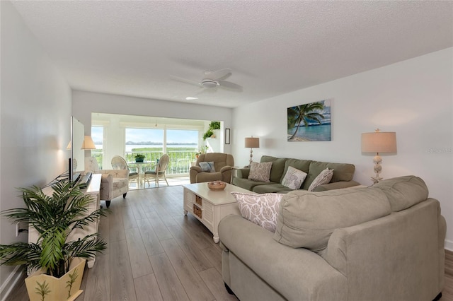 living room featuring light hardwood / wood-style floors, ceiling fan, and a textured ceiling