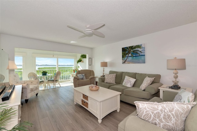 living room with a textured ceiling, light hardwood / wood-style flooring, and ceiling fan