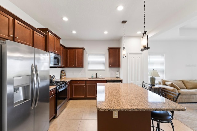 kitchen featuring sink, a kitchen breakfast bar, light stone countertops, pendant lighting, and appliances with stainless steel finishes