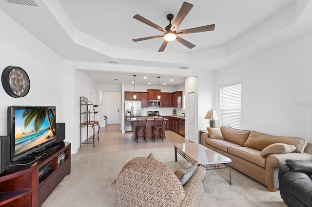 carpeted living room with a tray ceiling and ceiling fan