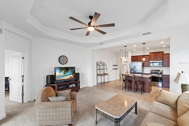 living room with ceiling fan, light colored carpet, and a raised ceiling