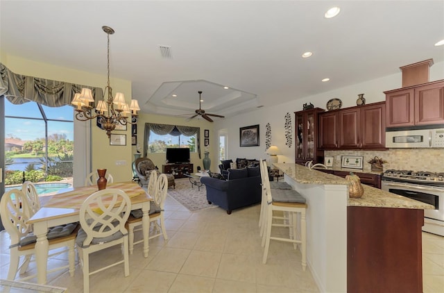 kitchen with stainless steel appliances, decorative light fixtures, decorative backsplash, a tray ceiling, and ceiling fan with notable chandelier