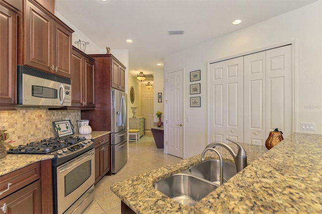 kitchen featuring tasteful backsplash, appliances with stainless steel finishes, light tile patterned floors, light stone countertops, and sink