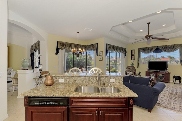 kitchen featuring light stone countertops, hanging light fixtures, sink, an island with sink, and a tray ceiling