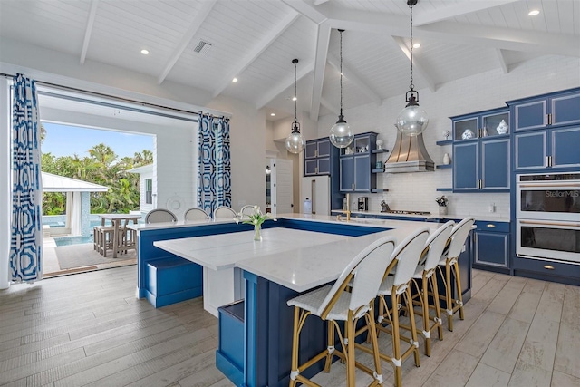 kitchen featuring light wood-type flooring, white double oven, a large island with sink, and blue cabinets