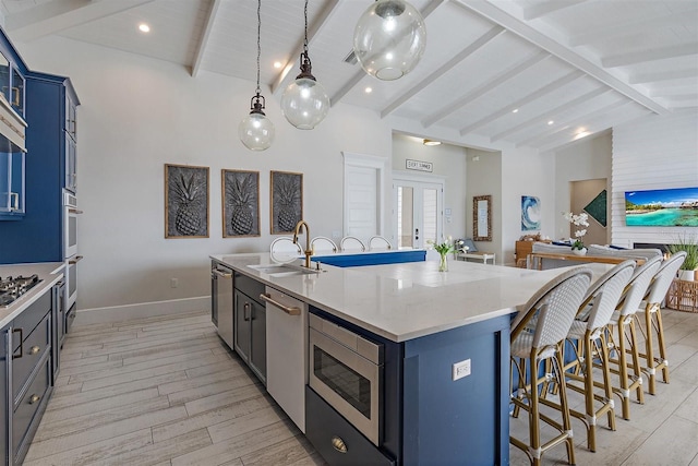 kitchen with lofted ceiling with beams, sink, hanging light fixtures, a kitchen island with sink, and appliances with stainless steel finishes