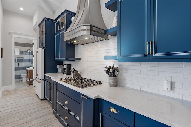 kitchen featuring high end fridge, stainless steel gas cooktop, light stone countertops, blue cabinetry, and island range hood