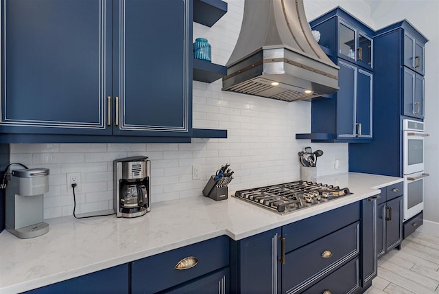 kitchen with island exhaust hood, blue cabinetry, stainless steel gas cooktop, and backsplash